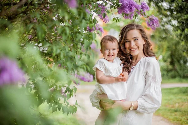 Vacker ung mor och dotter nära blommande lila. Våren. — Stockfoto