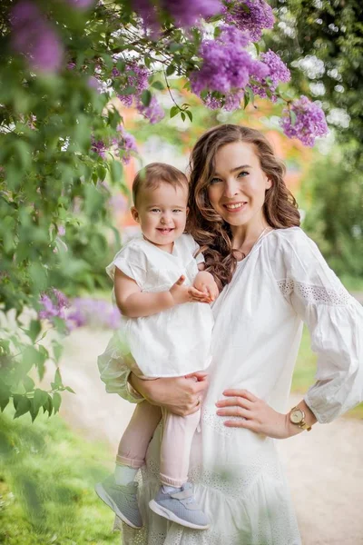 Hermosa joven madre e hija cerca de la floreciente lila. Primavera . —  Fotos de Stock