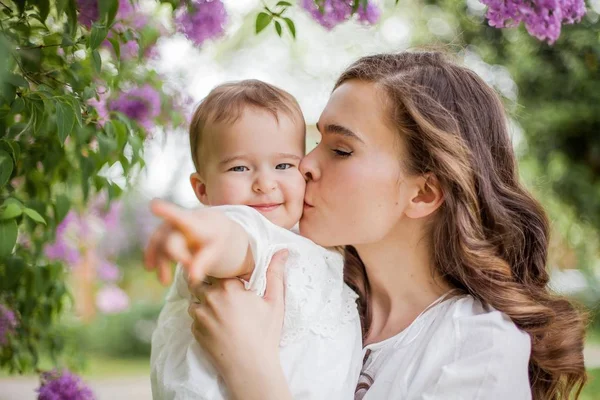 Bela jovem mãe e filha perto do lilás florescente. Primavera . — Fotografia de Stock