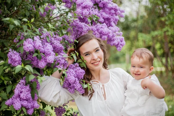 Beautiful young mother and daughter near the blossoming lilac. Spring. — Stock Photo, Image