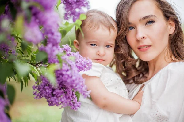 Bela jovem mãe e filha perto do lilás florescente. Primavera . — Fotografia de Stock