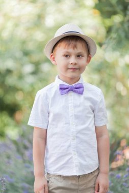 5 yaşında küçük bir çocuk çiçekli bir parkta yürüyor. Lavanta. Bahar. Papyon ile şapkalı bir çocuğun portresi.