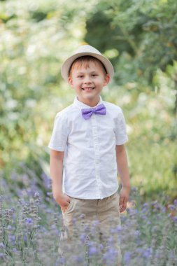 5 yaşında küçük bir çocuk çiçekli bir parkta yürüyor. Lavanta. Bahar. Papyon ile şapkalı bir çocuğun portresi.