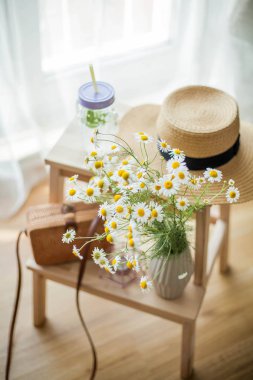 Küçük hasır kadın çantası, bir buket papatyalar, nane ile limonata, hasır şapka, ahşap sandalye. Bahar. Rahat.