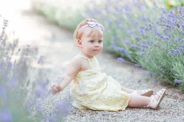 Niña de ojos azules sentada cerca de la floreciente lavanda. Cálido verano. Primavera . — Foto de Stock