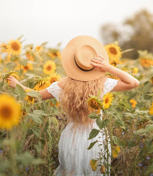 Schöne lockige junge Frau in einem Sonnenblumenfeld mit einem Weidenhut. Porträt einer jungen Frau in der Sonne. Sommer. — Stockfoto