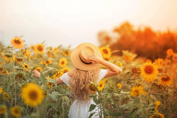 Bela jovem encaracolado em um campo de girassol segurando um chapéu de vime. Retrato de uma jovem ao sol. Verão . — Fotografia de Stock