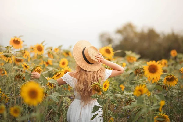 Schöne lockige junge Frau in einem Sonnenblumenfeld mit einem Weidenhut. Porträt einer jungen Frau in der Sonne. Sommer. — Stockfoto