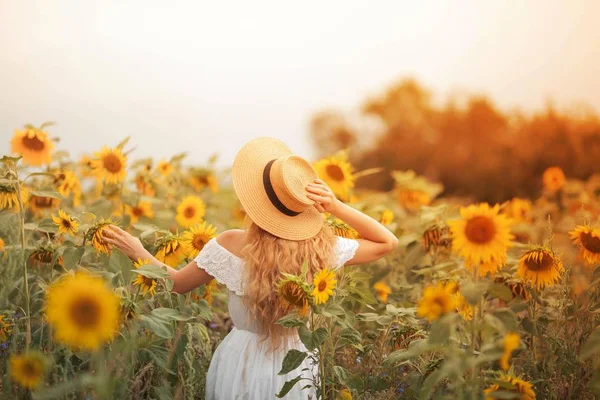 Bela jovem encaracolado em um campo de girassol segurando um chapéu de vime. Retrato de uma jovem ao sol. Verão . — Fotografia de Stock