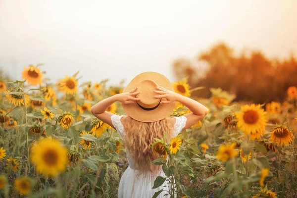 Bela jovem encaracolado em um campo de girassol segurando um chapéu de vime. Retrato de uma jovem ao sol. Verão . — Fotografia de Stock