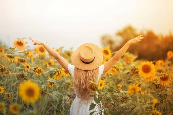 Bela jovem encaracolado em um campo de girassol segurando um chapéu de vime. Retrato de uma jovem ao sol. Verão . — Fotografia de Stock