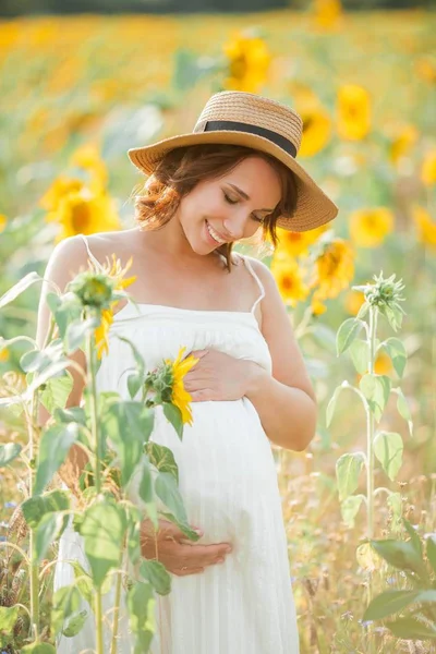 Schöne junge schwangere Frau im Sonnenblumenfeld. Porträt einer jungen Schwangeren in der Sonne. Sommer. — Stockfoto