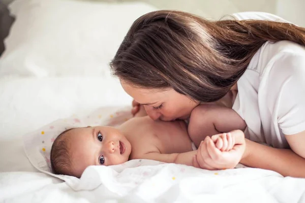 Tânăra mamă frumoasă ţine un copil. Mama îşi sărută copilul. Dormitor pentru copii . — Fotografie, imagine de stoc