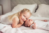 Mladá krásná matka drží dítě. Malá sestřička líbá svou malou sestru. Dítě. Dětská ložnice.