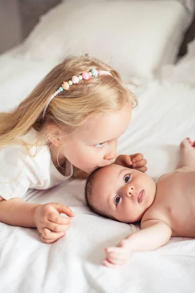 若い美しい母親が赤ん坊を抱いている。妹は妹にキスをする。赤ちゃん。子供用ベッドルーム. — ストック写真