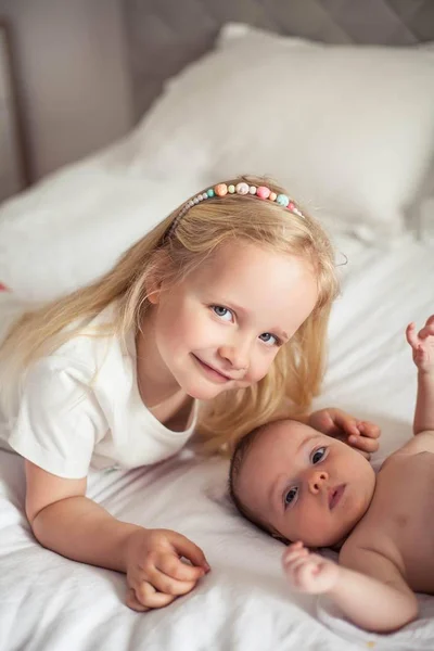 Η νεαρή όμορφη μητέρα κρατά ένα μωρό. Η αδελφούλα φιλάει τη μικρή της αδερφή. Μωρό. Παιδικό υπνοδωμάτιο. — Φωτογραφία Αρχείου
