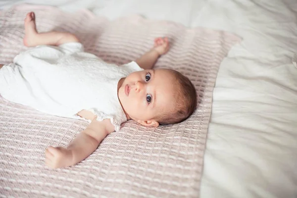 Ένα μικρό χαριτωμένο κορίτσι 3 μηνών είναι ξαπλωμένο στο κρεβάτι. Μωρό. Παιδικό υπνοδωμάτιο. — Φωτογραφία Αρχείου