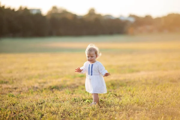 Una niña rizada de ojos azules con un vestido blanco camina por el campo. Retrato de una niña al sol. Puesta de sol . —  Fotos de Stock