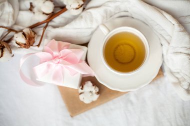 Çay, pamuk, ekose, kitap ve yatakta pembe bir kurdele ile beyaz hediye kutusu ile beyaz kupa. Yatakta kahvaltı. Rahat. Sonbahar. Kış.