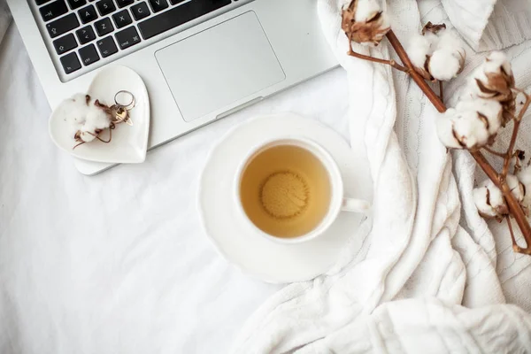 Tazza bianca con tè, cotone, laptop, plaid sul letto. Colazione a letto. Accogliente. Autunno. Inverno . — Foto Stock