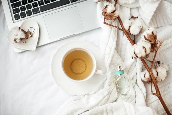 白いマグカップ(紅茶、コットン、ノートパソコン、チェック柄、キャンドル、本付き)がベッドの上に立っています。ベッドで朝食。居心地。秋。冬. — ストック写真