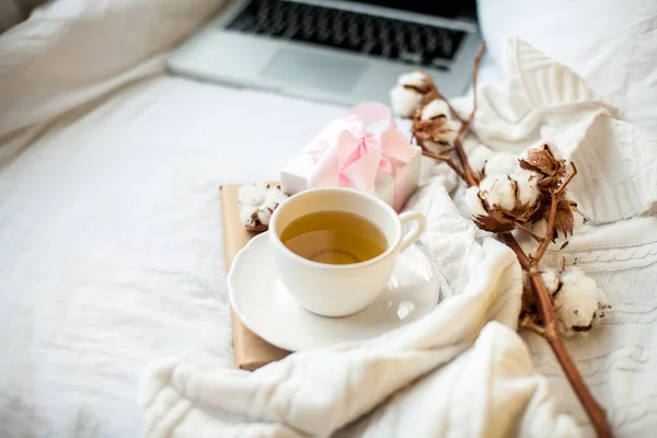 ベッドの上にピンクのリボンが付いている紅茶、綿、ノート、チェック、本と白のギフトボックスと白いマグカップ。ベッドで朝食。居心地。秋。冬. — ストック写真