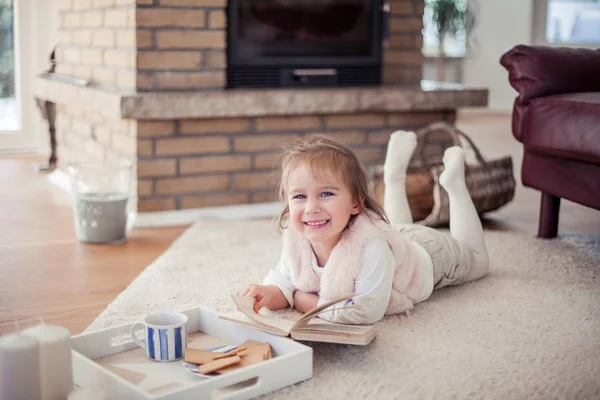 Bella bambina sta leggendo un libro vicino al camino. Accogliente. Autunno . — Foto Stock