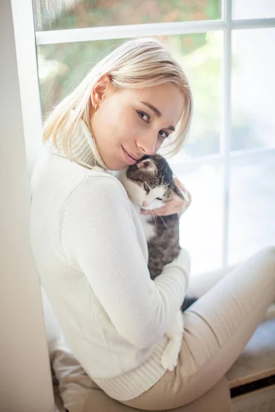 Die schöne junge Frau sitzt am Fenster und umarmt eine Katze. cozy.fall. — Stockfoto