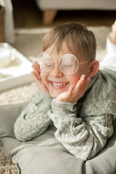 En vacker liten pojke i en stickad tröja läser av fönstret med en mugg hett te. Mysiga. Hösten. — Stockfoto