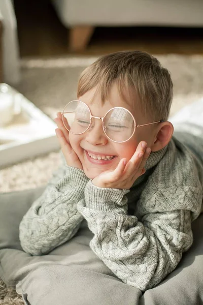 En vacker liten pojke i en stickad tröja läser av fönstret med en mugg hett te. Mysiga. Hösten. — Stockfoto