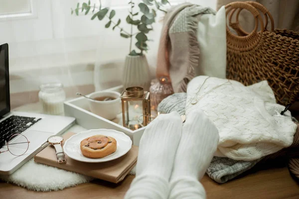 Foto tonica. Arredo autunnale. Gambe di donna in calzini lavorati a maglia, un computer portatile, una tazza di tè caldo, un panino, candele. Accogliente. Autunno . — Foto Stock