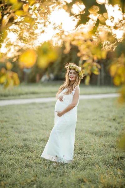 Porträtt av en gravid kvinna i solen. Ung vacker gravid kvinna med en krans på huvudet på fältet. Moderskap. Varm höst. — Stockfoto