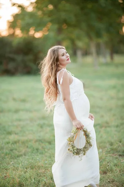 Portrait of a pregnant woman in the sun. Young beautiful pregnant woman with a wreath on her head in the field. Motherhood. Warm autumn. — Stock Photo, Image