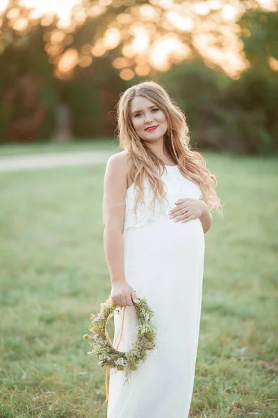 Porträt einer schwangeren Frau in der Sonne. junge schöne schwangere Frau mit einem Kranz auf dem Kopf auf dem Feld. Mutterschaft. warmer Herbst. — Stockfoto