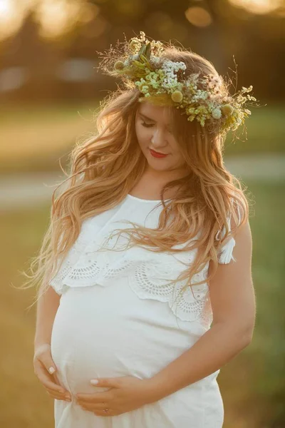 Porträt einer schwangeren Frau in der Sonne. junge schöne schwangere Frau mit einem Kranz auf dem Kopf auf dem Feld. Mutterschaft. warmer Herbst. — Stockfoto