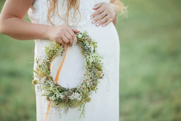 Close-up. Retrato de uma mulher grávida ao sol. Jovem mulher grávida bonita com uma coroa de flores na cabeça no campo. Maternidade. Outono quente . — Fotografia de Stock