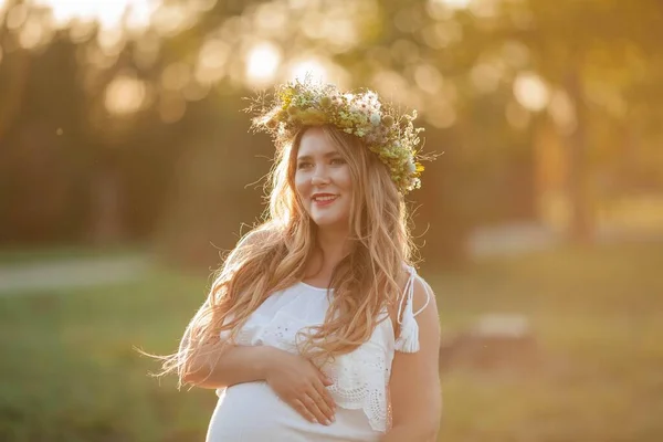 太陽の下で妊婦の肖像画。フィールドに彼女の頭の上に花輪を持つ若い美しい妊婦。母親。暖かい秋. — ストック写真