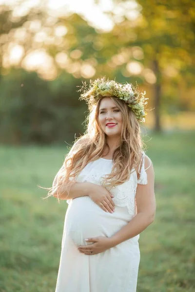 Ritratto di donna incinta al sole. Giovane bella donna incinta con una corona di fiori in testa sul campo. La maternità. Autunno caldo . — Foto Stock