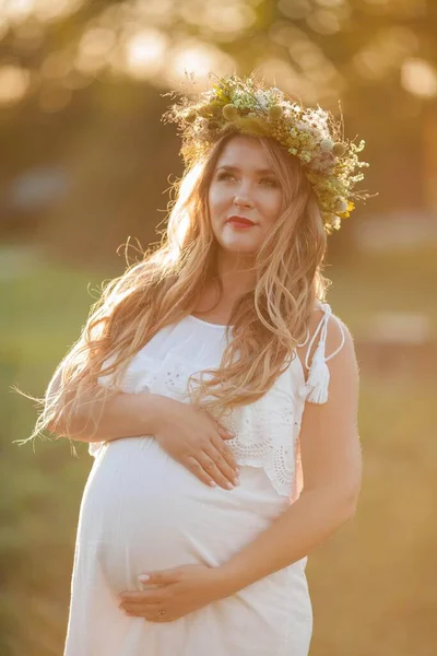 Porträtt av en gravid kvinna i solen. Ung vacker gravid kvinna med en krans på huvudet på fältet. Moderskap. Varm höst. — Stockfoto