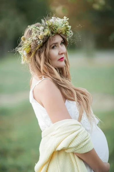 Porträt einer schwangeren Frau in der Sonne. junge schöne schwangere Frau mit einem Kranz auf dem Kopf auf dem Feld. Mutterschaft. warmer Herbst. — Stockfoto