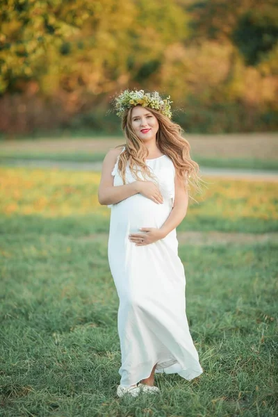 Porträtt av en gravid kvinna i solen. Ung vacker gravid kvinna med en krans på huvudet på fältet. Moderskap. Varm höst. — Stockfoto