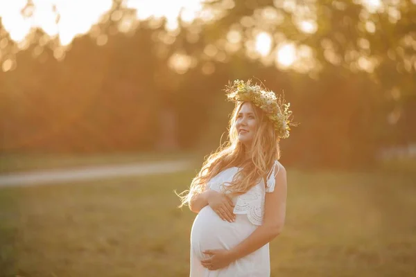 Porträtt av en gravid kvinna i solen. Ung vacker gravid kvinna med en krans på huvudet på fältet. Moderskap. Varm höst. — Stockfoto