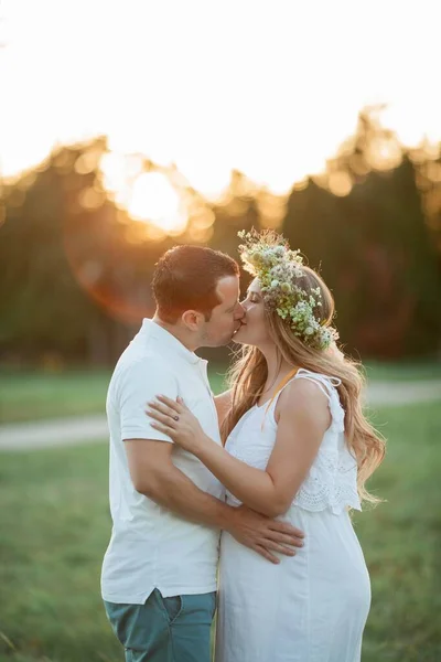 Young beautiful couple expecting a baby. Young beautiful pregnant woman with a wreath on her head holds on to a belly. Motherhood. Warm autumn. — Stock Photo, Image