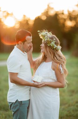 Bebek bekleyen genç ve güzel bir çift. Kafasında çelenk olan güzel hamile bir kadın karnına tutunuyor. Annelik. Sıcak sonbahar.