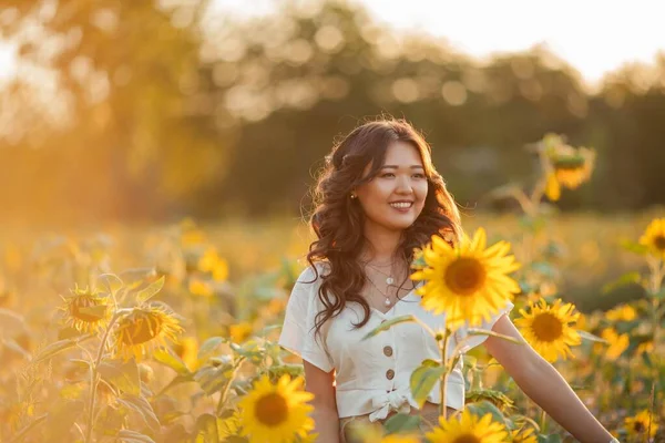 Mladá Asiatka s kudrnatými vlasy na poli slunečnic při západu slunce. Portrét mladé krásné asijské ženy na slunci. — Stock fotografie