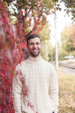 Kırmızı yapraklı bir ağacın yanında genç bir adamın portresi. Sonbahar.