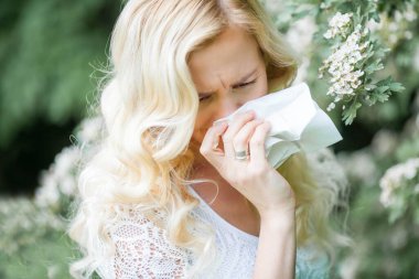 Alerjisi olan genç ve güzel bir sarışının portresi. Beyaz çiçeklerin yanında genç bir kadının bahar portresi. Alerji..