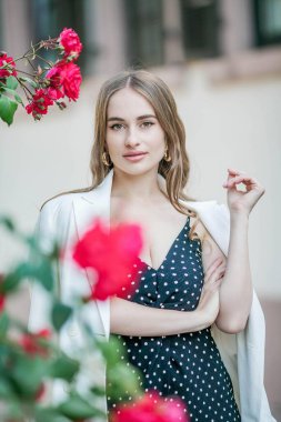 Genç ve güzel bir kadın bir Avrupa şehrinde yürüyor. Çiçek açan güllerin yanında genç bir kadının portresi. Avrupa.