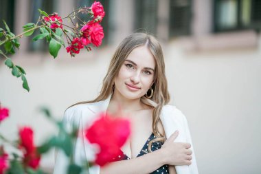 Genç ve güzel bir kadın bir Avrupa şehrinde yürüyor. Çiçek açan güllerin yanında genç bir kadının portresi. Avrupa.