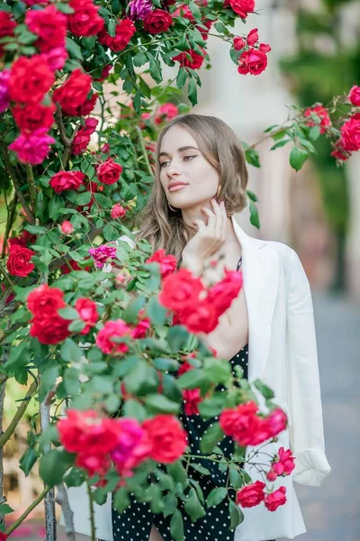 Jovem mulher bonita caminha em uma cidade europeia. Retrato de uma jovem perto de rosas em flor. A Europa . — Fotografia de Stock